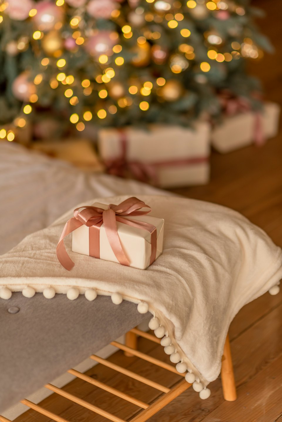 Wrapped gift with a rose gold ribbon sits on a textured blanket.
